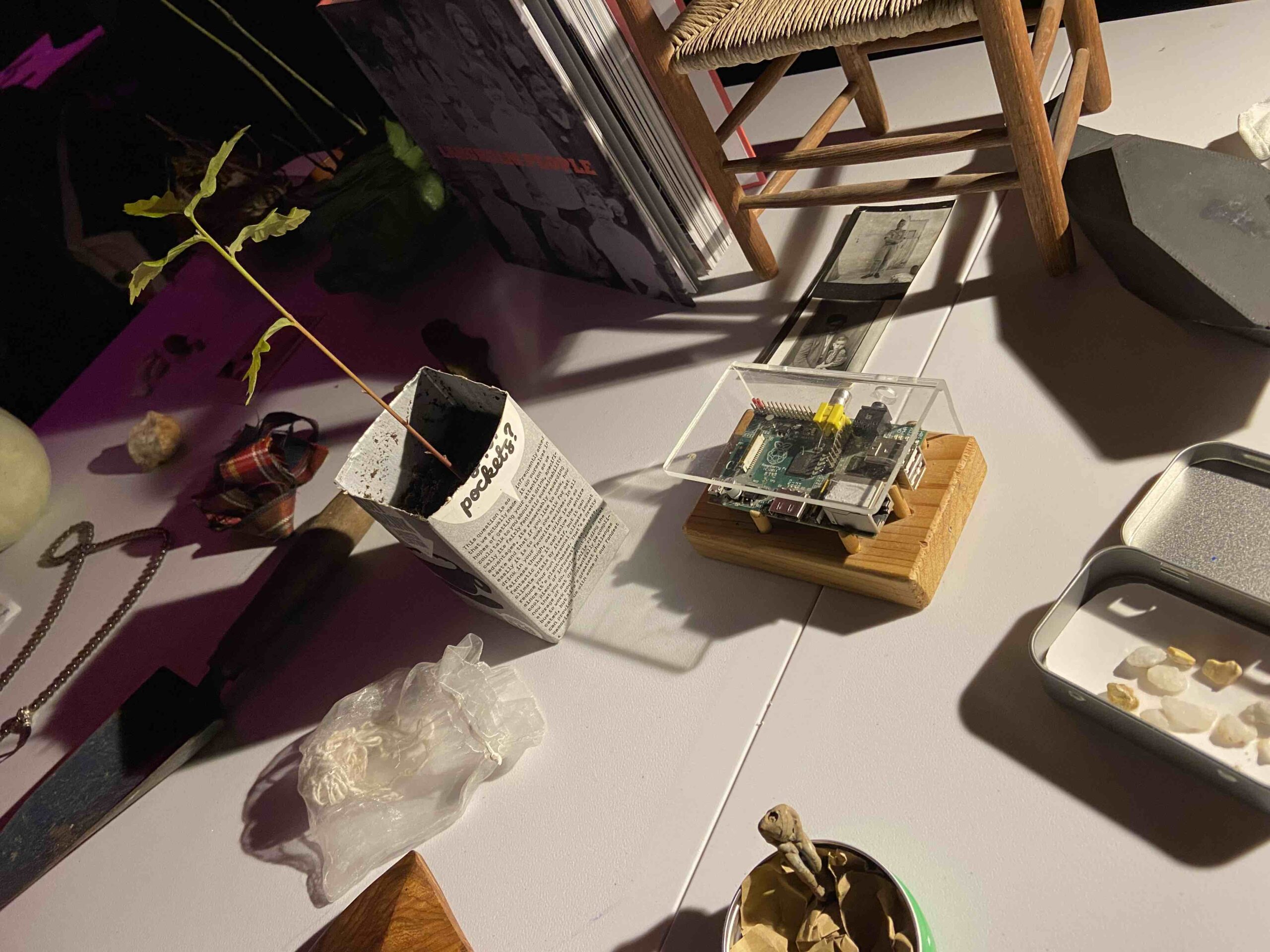 Photograph of a selection of objects laid on a table: a raspberry pi computer, an oak sapling, a book, a miniature wooden chair, an old family photograph, a piece of tartan, and tin with some interesting stones in.